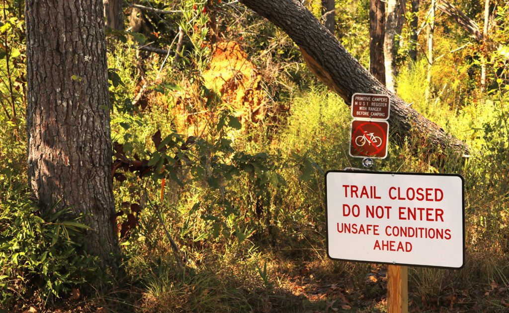 Sign that trail is closed in front of fallen trees and debris.